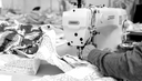 A close-up of a sewing machine with a person sewing fabric, surrounded by various textiles.